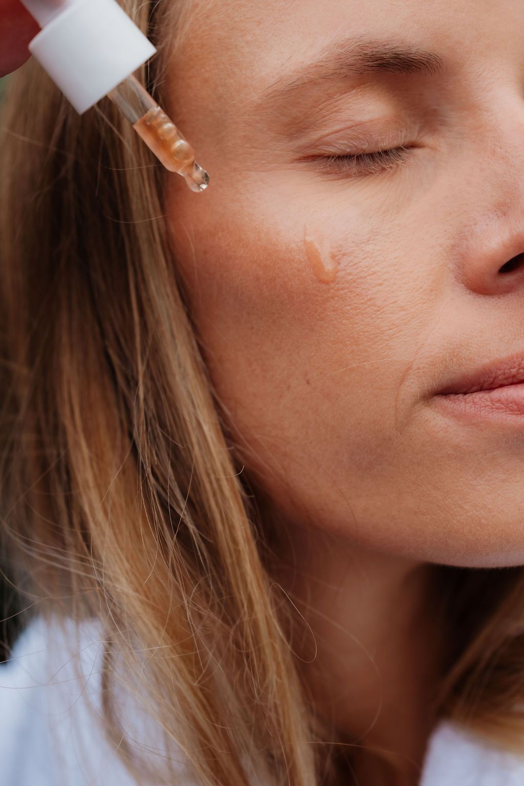 Close-up of a dropper releasing a drop of serum onto a woman's cheek